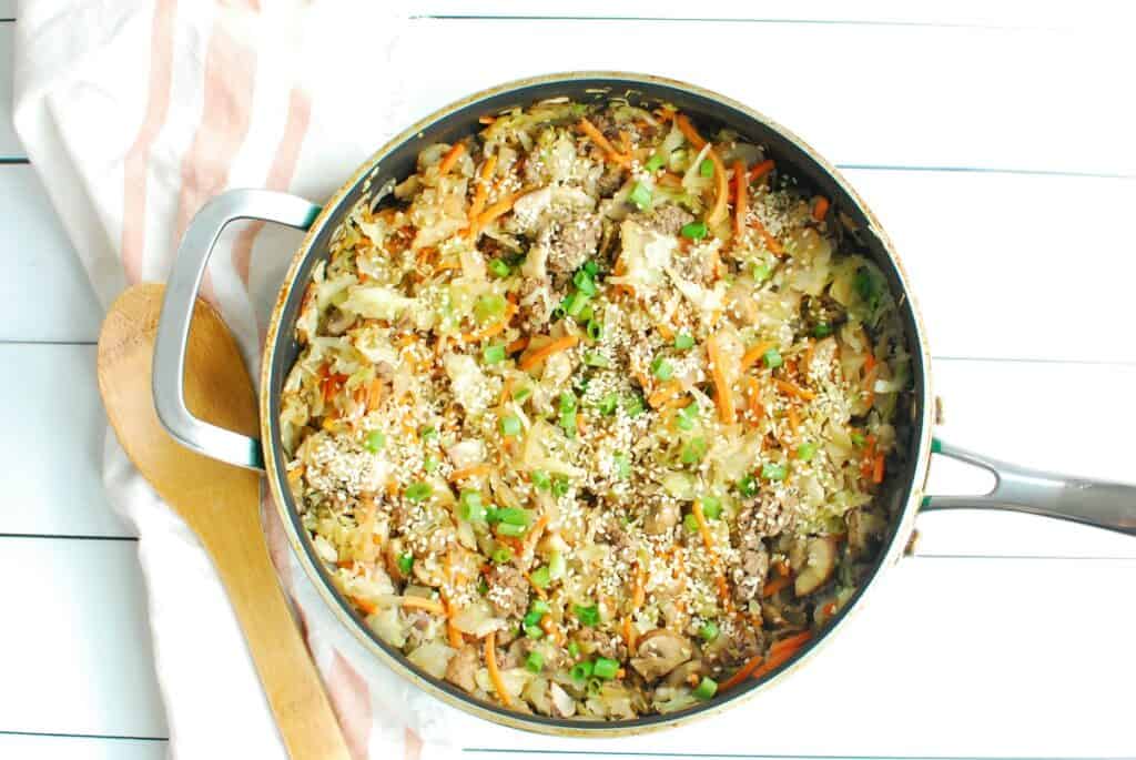 Egg roll in a bowl in a pan next to a wooden spoon.