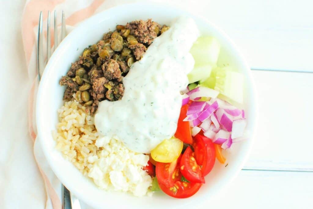 Greek beef bowl with rice, beef, lentils, tomatoes, cucumber, red onion, and Greek yogurt sauce.