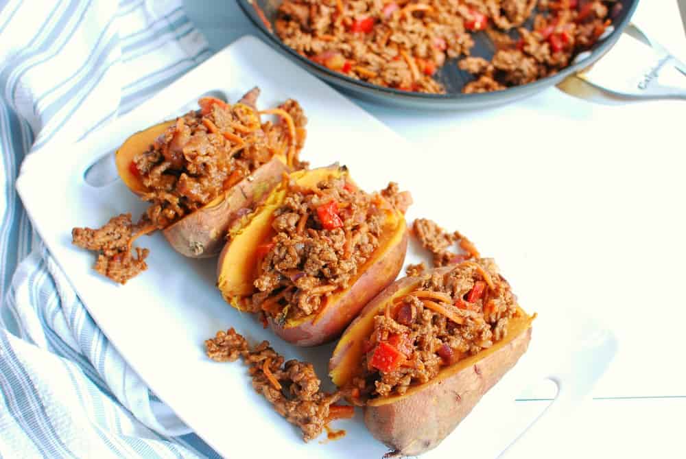 Three ground beef stuffed sweet potatoes on a white platter.