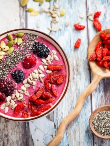 A smoothie bowl topped with goji berries, pumpkin seeds, chia seeds, and berries.