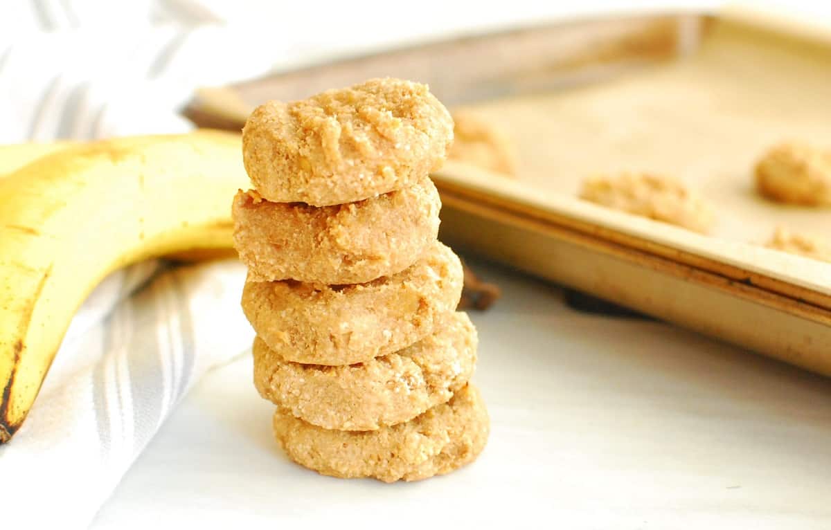 A stack of peanut butter banana cookies next to a banana and a baking sheet.