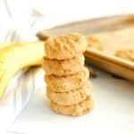 Several banana peanut butter cookies stacked in a row, next to a banana and a napkin.