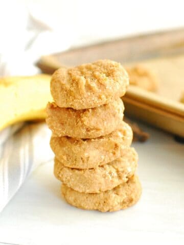 Several banana peanut butter cookies stacked in a row, next to a banana and a napkin.