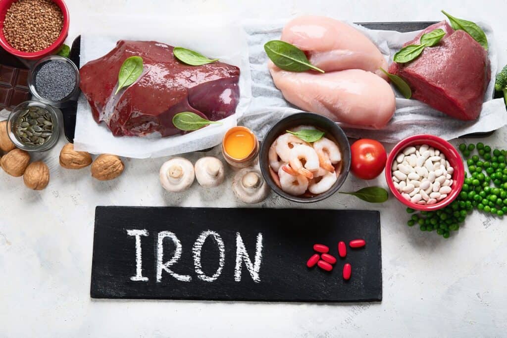 A table full of foods like liver, chicken, beef, nuts, mushrooms, and seeds, with a iron slate that says "iron" on it.