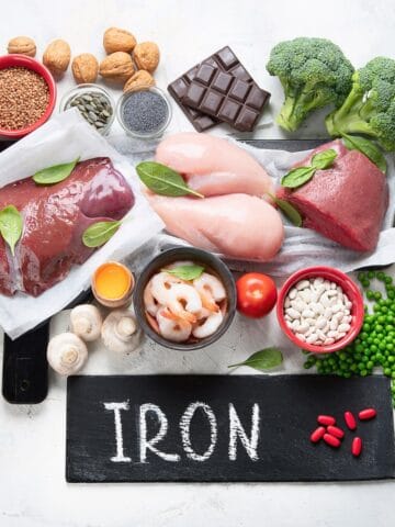 Iron rich foods like beef, liver, chicken, eggs, and greens on a table.