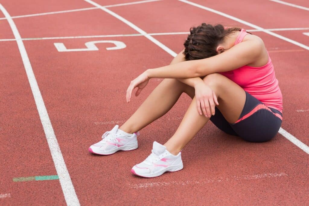 A tired female athlete sitting on the track.