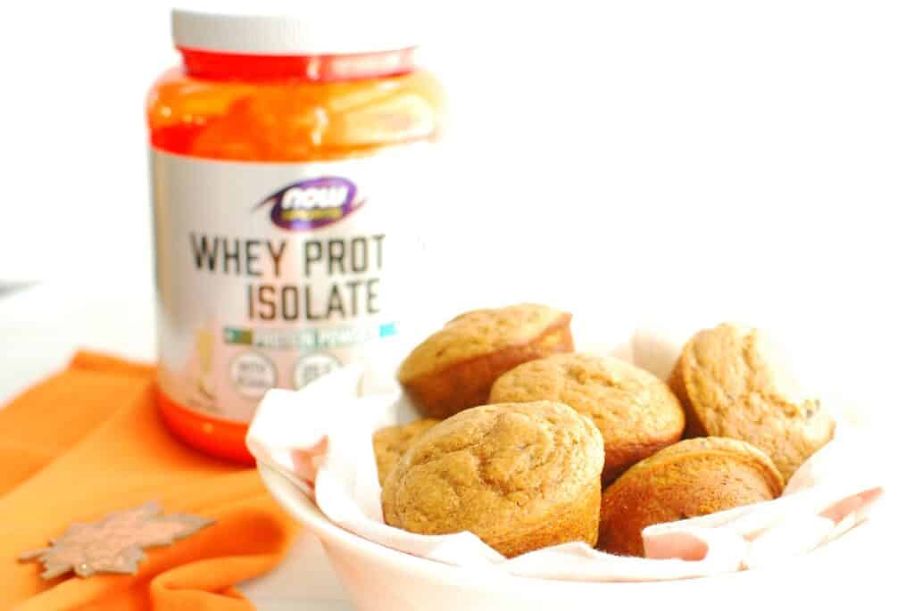 A bowl of pumpkin protein muffins next to a container of protein powder.