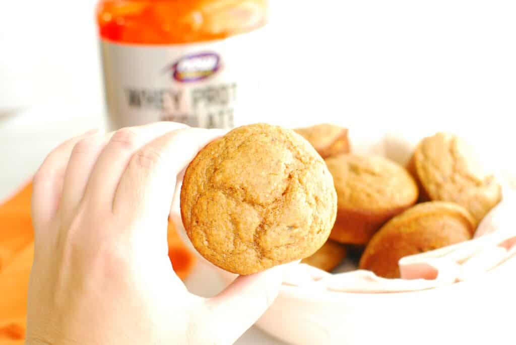 A woman's hand holding a pumpkin protein muffin.