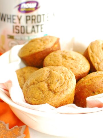 A bowl filled with pumpkin protein muffins, next to an orange napkin.