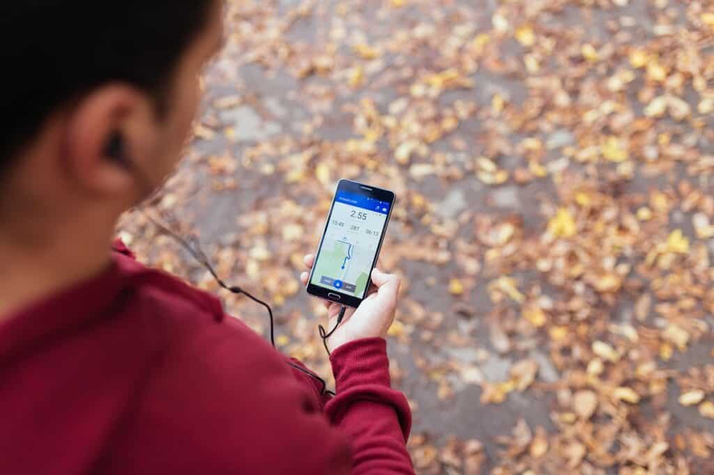 A man looking down at his phone while out on a fall run.