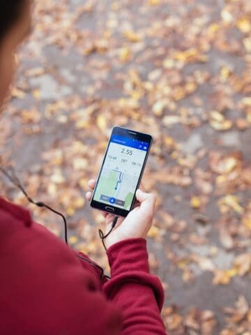 A man looking down at his phone while out on a fall run.