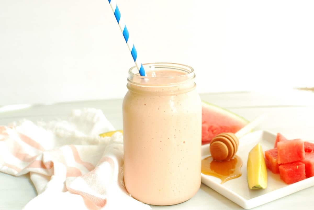 A watermelon protein smoothie in a mason jar with a straw.