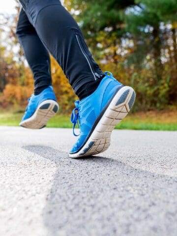 A woman's legs with blue sneakers running outside on pavement.