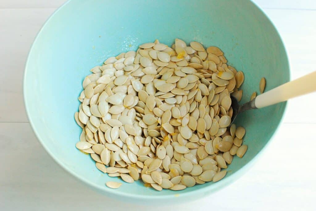 Pumpkin seeds in a bowl mixed together with oil, salt, and garlic powder.