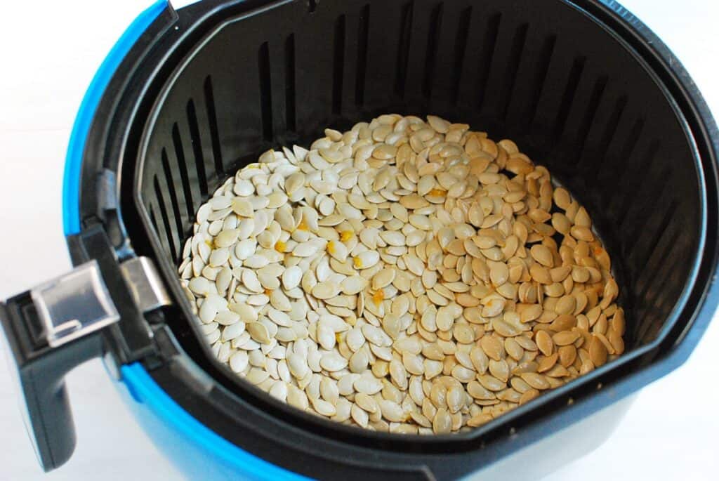 Uncooked pumpkin seeds in an air fryer basket. 