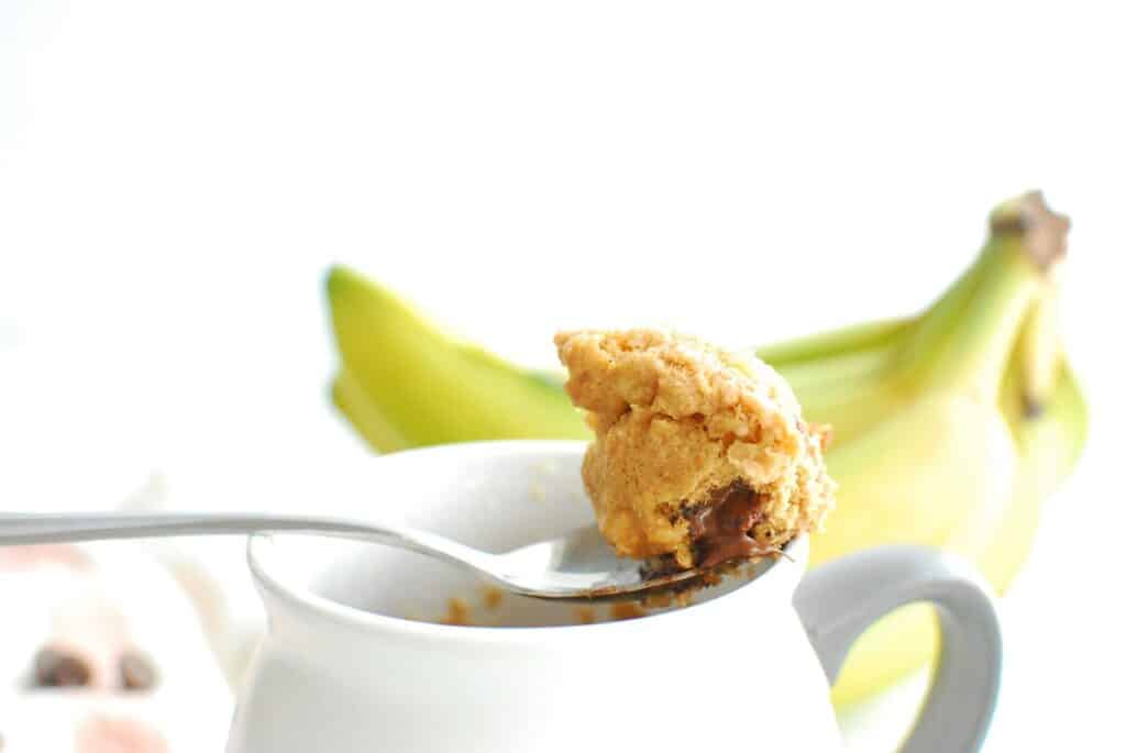 A spoonful of banana mug cake sitting on top of the mug.