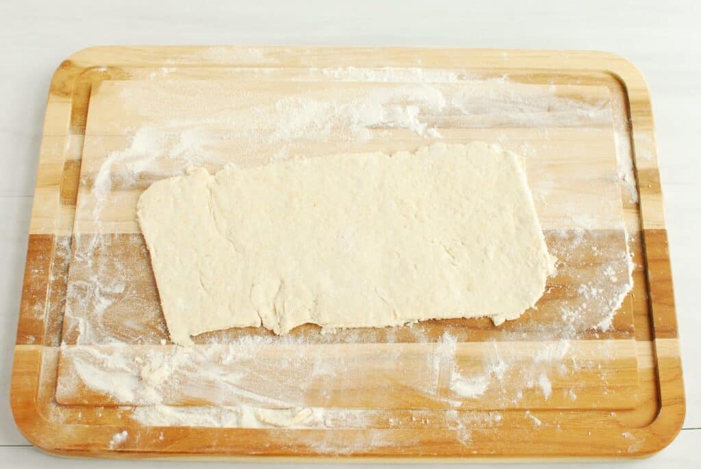 A pizza crust rolled out on a floured cutting board.