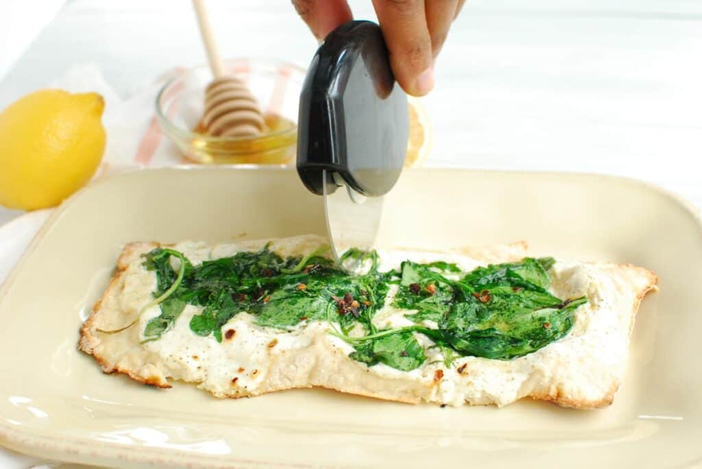 A man's hand rolling a pizza cutter over a lemon ricotta pizza.