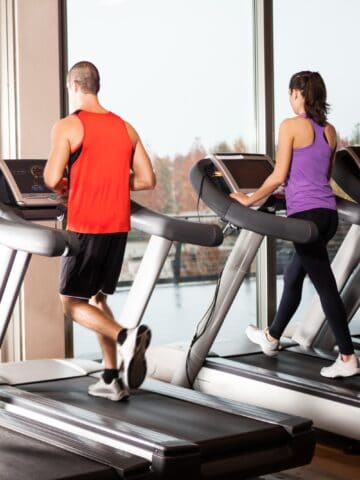 Two people running on treadmills at a gym.