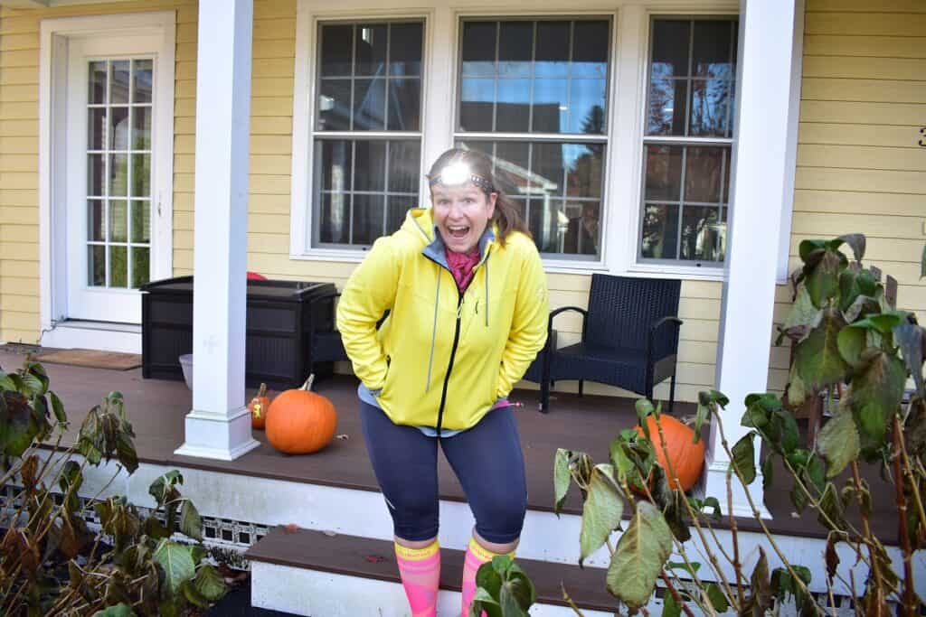 A woman wearing a headlight outside in front of a house.