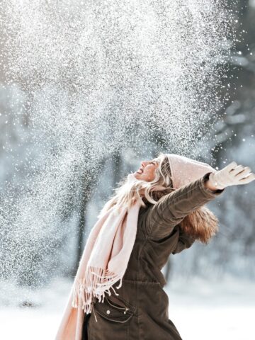A woman outside during the holidays in snow, throwing her hands in the air.