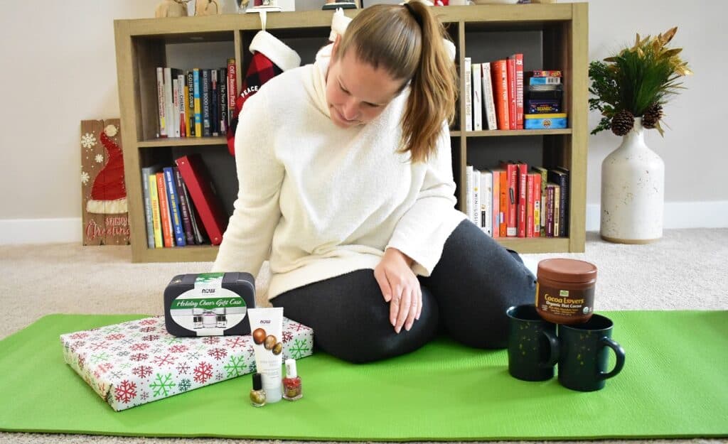 A woman sitting on a yoga mat with self care products, with holiday decorations in the background.