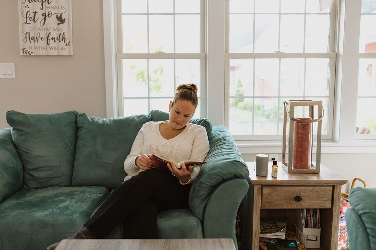 A woman reading a book on a turquoise couch.