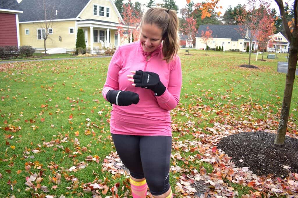 A woman outside in running clothes and convertible mittens.