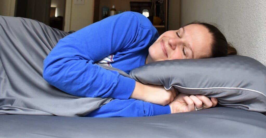 A woman sleeping on a bed with grey sheets.