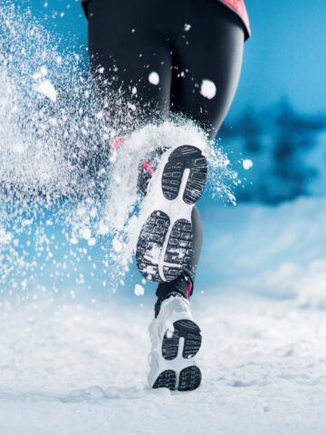 A woman running outside on a snowy day, focused on her sneakers.