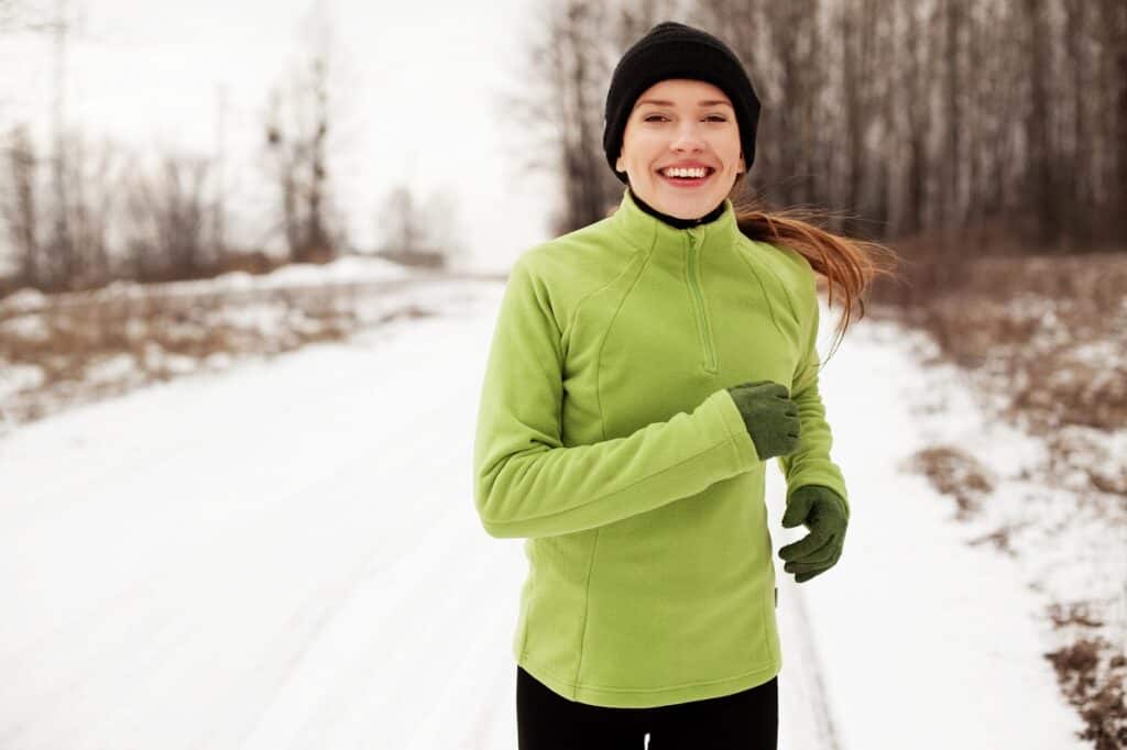 A woman running outside on a snowy road in cold weather.