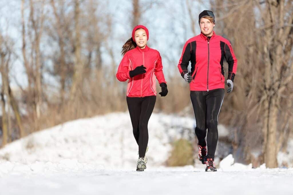 A man and a woman running outside on a winter day in the cold.