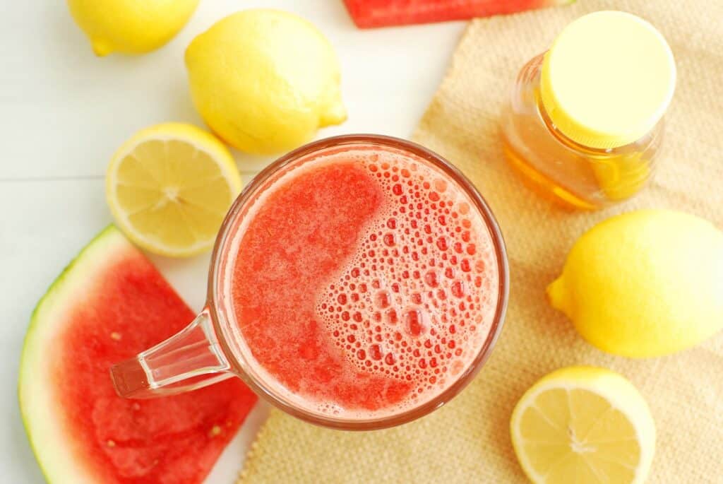 Overhead shot of a mug of warm watermelon lemonade, next to some fresh lemons.