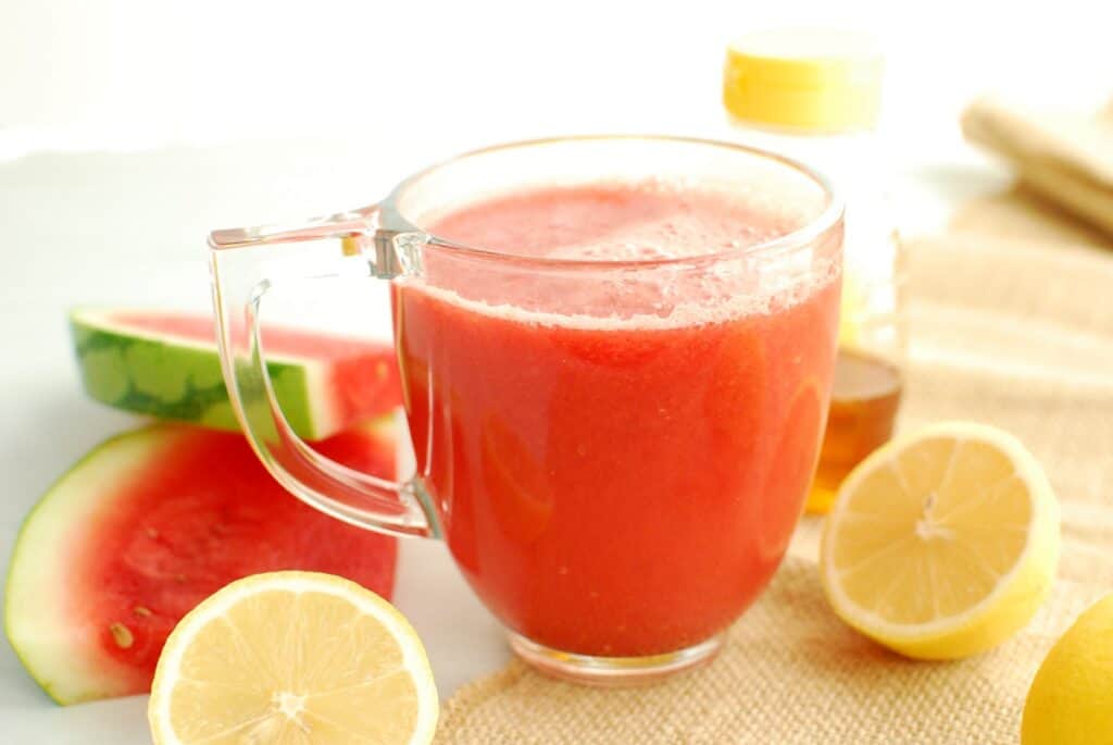 A mug filled with hot watermelon lemonade next to fresh lemons and a slice of watermelon.