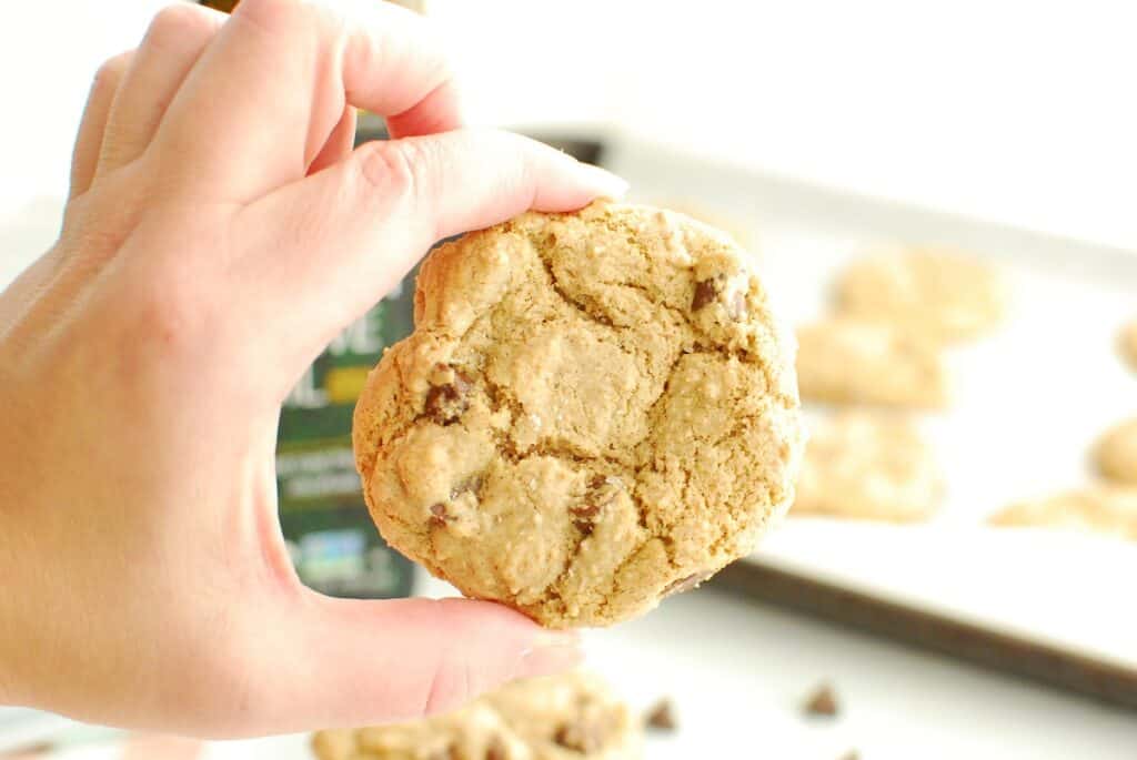 A woman's hand holding a chocolate chip cookie made with olive oil.