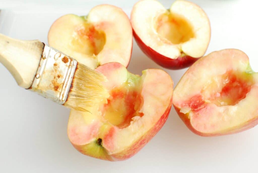 Apple halves being brushed with butter.