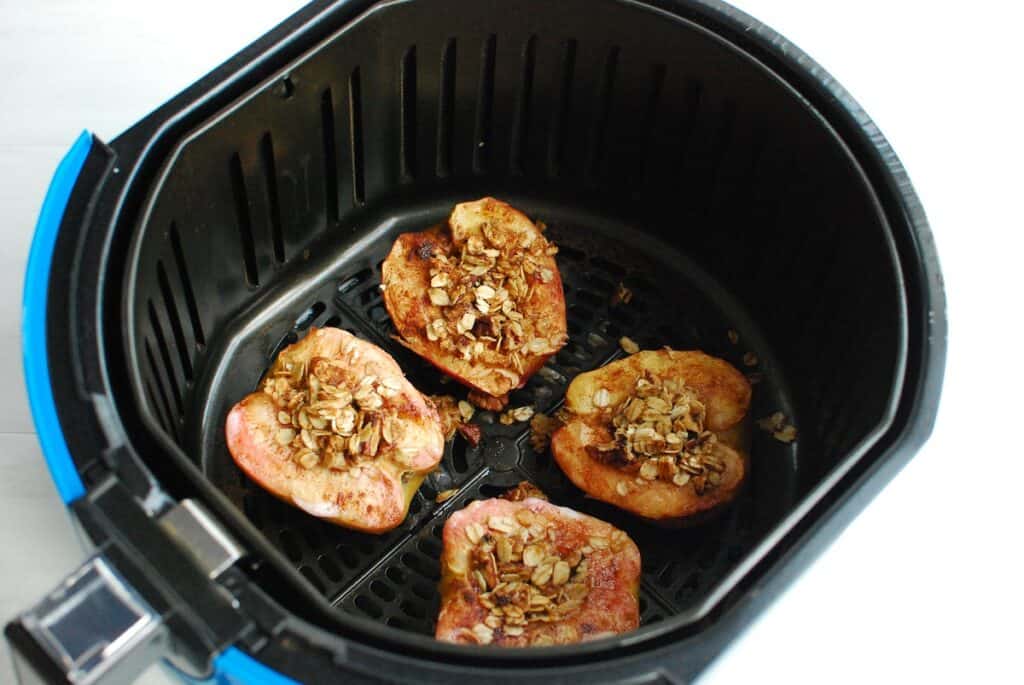 Baked apples that have been cooked sitting in an air fryer basket.