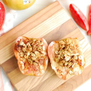 Two air fryer baked apples on a small wooden cutting board.