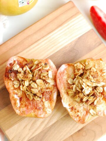 Two air fryer baked apples on a small wooden cutting board.