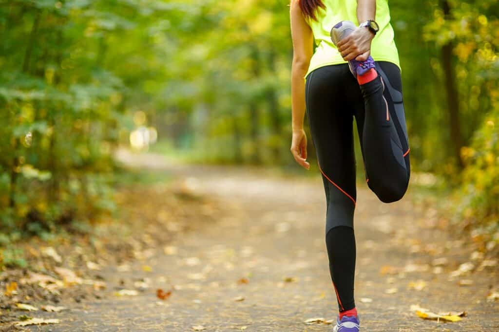 A woman in athletic clothes stretching her legs outside.