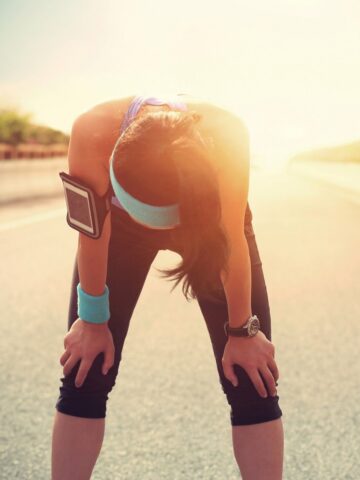 A woman outside on a sunny day taking a break from her run because her legs are tired.