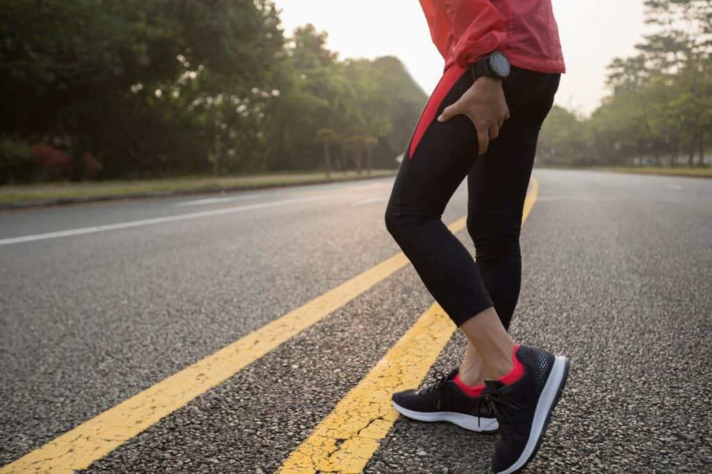 A woman taking a break from her run outside due to heavy legs.