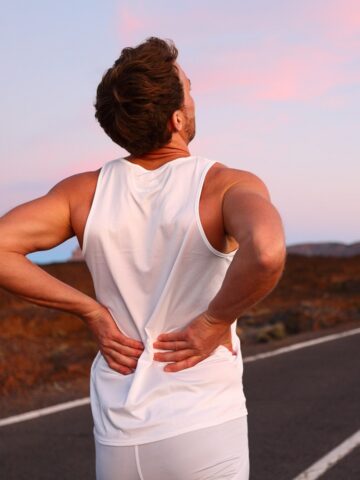 A runner outside, paused from their workout, holding their back.
