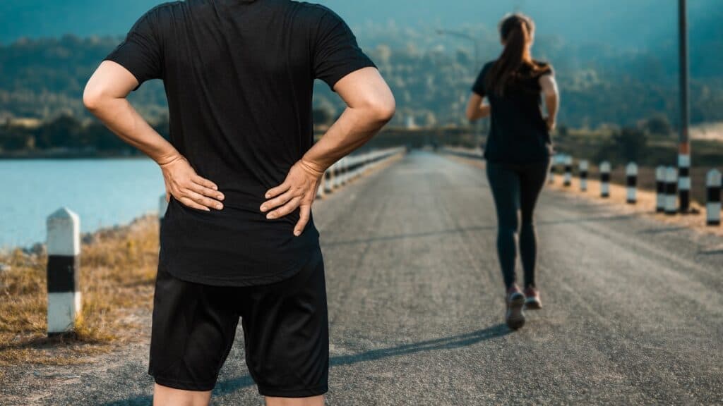 A man pausing on his run with a little lower back pain related to lower cross syndrome.