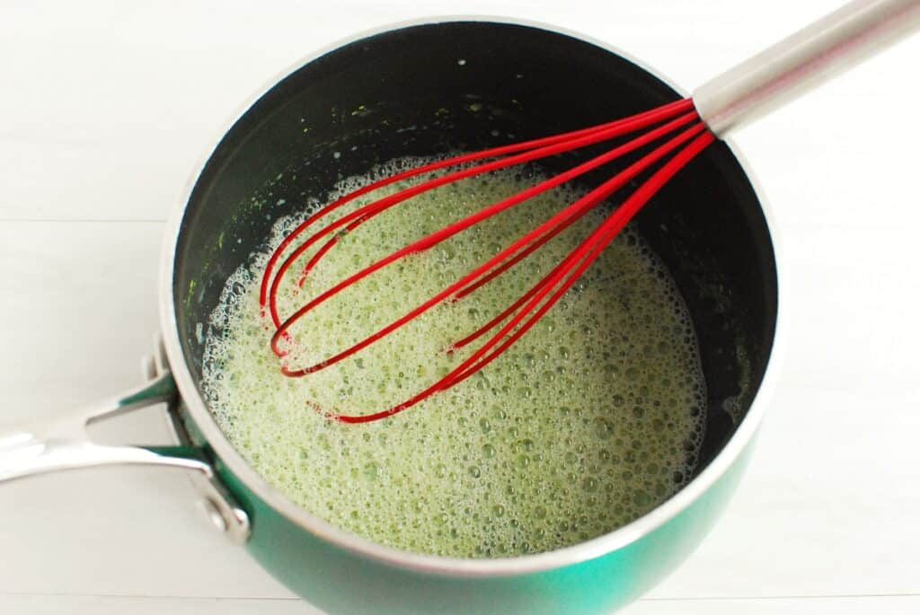 Milk and matcha powder whisked together in a small pot.