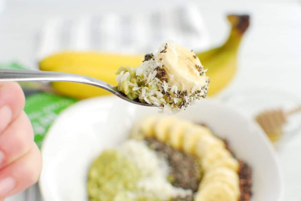 A spoonful of oatmeal topped with banana, coconut, chia seeds, and cacao nibs.