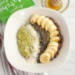 A bowl of matcha oatmeal topped with a banana, chia seeds, coconut, and cacao nibs.
