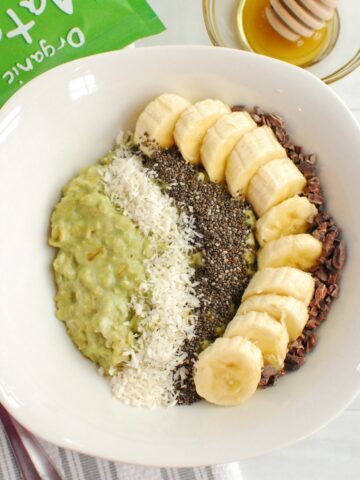 A bowl of matcha oatmeal topped with a banana, chia seeds, coconut, and cacao nibs.