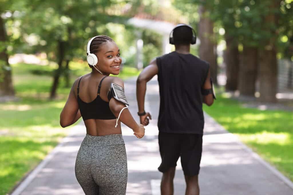 A woman running outside, smiling back at the camera, listening to a running podcast.