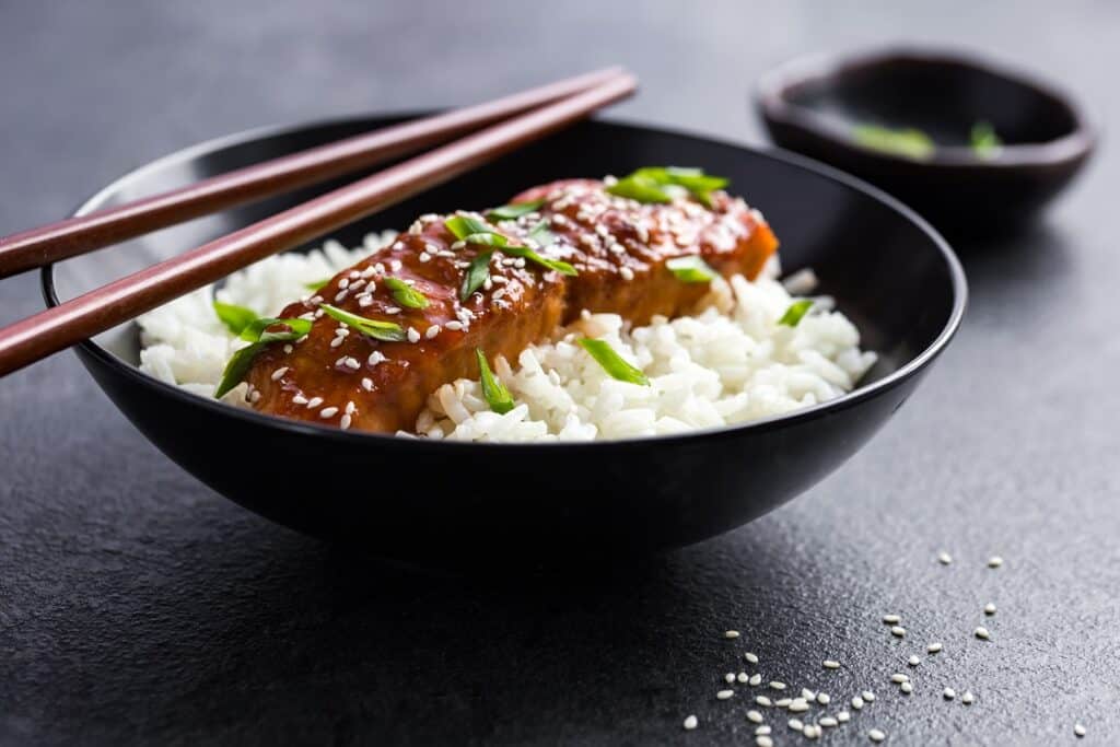 A bowl of salmon and rice with chopsticks on top.